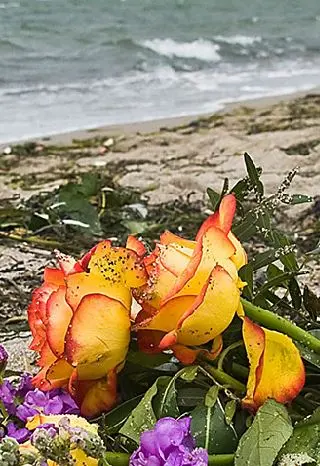 Blumenstrauss mit violetten Blüten und orangefarbenen Rosen, im Hintergrund das Meer
